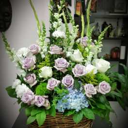 Basket arrangement of lavender and white roses with blue hydrangea