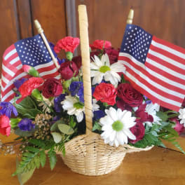 Basket arrangement of red roses, carnations, and white daisies with two American flags