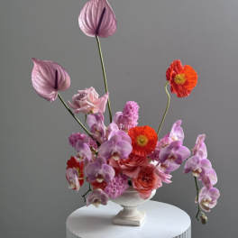 Pink and red floral arrangement in a white pedestal vase