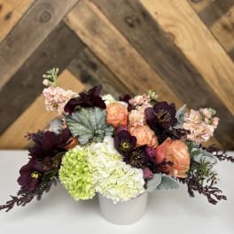 Bouquet of peach roses, hydrangeas, and dark purple blooms in a white vase