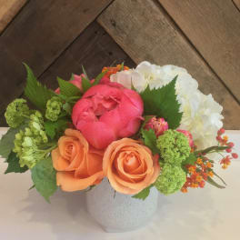 Mixed bouquet of pink, orange, and white flowers in a white vase
