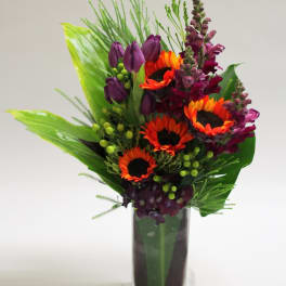 Bright bouquet of orange sunflowers and purple blooms in a clear glass vase
