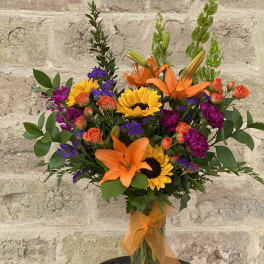 Bouquet of orange lilies, sunflowers, and purple flowers in a glass vase