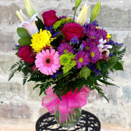 Mixed bouquet of pink roses, lilies, daisies, and mums in a glass vase with a bright pink bow