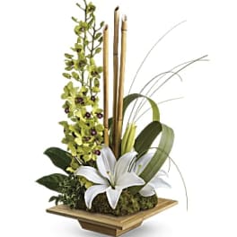 White lilies with green orchids and bamboo in a wooden container