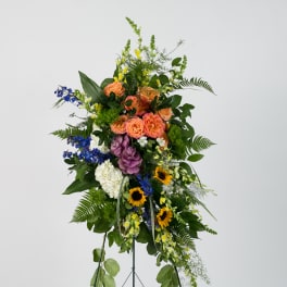 Tall standing floral spray with mixed blooms in peach, blue, yellow, white, and purple