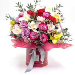 Bouquet of roses and orchids in a pink hatbox with a ribbon