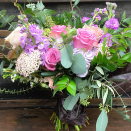 Bouquet of pink and purple roses with mixed greenery and brown wrapping