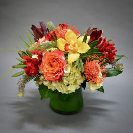 Colorful bouquet in a green glass vase with yellow orchids and orange roses
