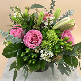 Pink roses and lilies arranged in a low vase with white filler flowers