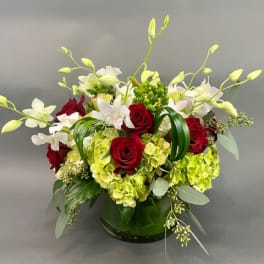 Red roses and white orchids arranged with green hydrangeas in a glass vase