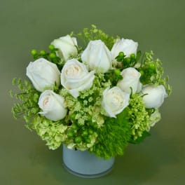 White roses and green flowers arranged in a pale blue vase