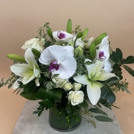 White lilies and orchids arranged in a green glass vase