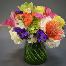 Colorful bouquet with roses, calla lilies, and a protea in a glass vase