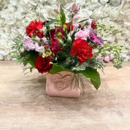 Red and pink mixed flower arrangement in a pink vase with a heart accent