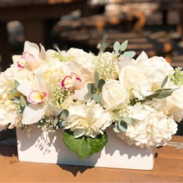 White floral arrangement in a rectangular vase with orchids and roses