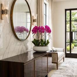 Pink orchid arrangement in a white bowl on a dark console table