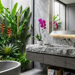 Potted purple orchid on a stone bathroom counter beside a mirror.