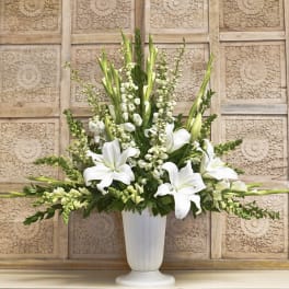 White lilies and tall white blooms arranged in a white pedestal vase