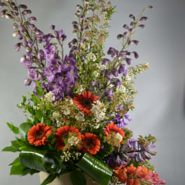 Tall mixed flower arrangement in a woven basket with orange and purple blooms