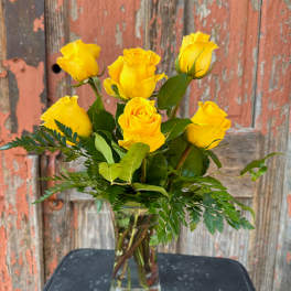 Yellow roses in a clear glass vase with greenery
