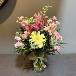 Pink and yellow flower arrangement in a glass vase with a ribbon