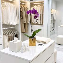Purple orchid in a gold pot on a white island in a walk-in closet.