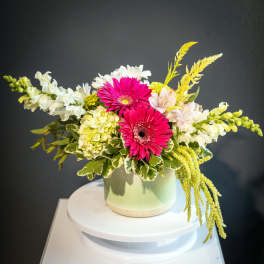 Pink gerbera daisies and white flowers arranged in a pale green vase