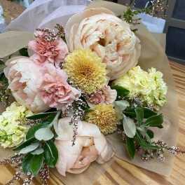 Pastel bouquet with large blush peonies and yellow blooms wrapped in paper