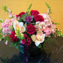 Mixed bouquet of red roses, pink hydrangeas, and white orchids in a black vase