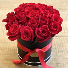 Red roses arranged in a black round box with a red ribbon