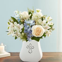 White and blue floral arrangement in a white vase with a cross emblem