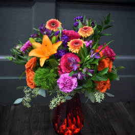Bright mixed bouquet in a red glass vase with orange, pink, and purple flowers.