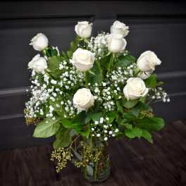 Tall arrangement of white roses and small white filler flowers in a clear glass vase.