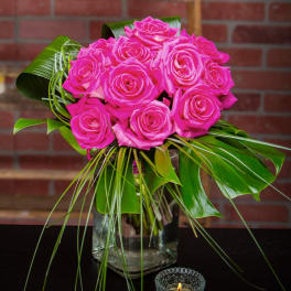 Hot pink roses arranged in a clear glass vase with tropical leaves