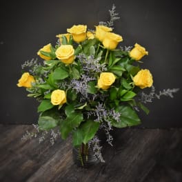 Arrangement of yellow roses with soft purple filler in a clear glass vase