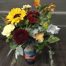 Mixed bouquet with sunflowers, red roses, and carnations in a colorful vase
