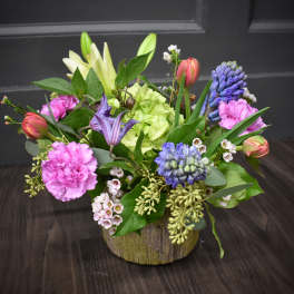 Mixed bouquet with pink carnations, lilies, and blue hyacinths in a rustic container