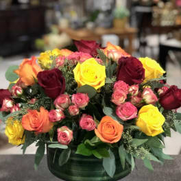 Mixed roses in a low green vase with pink, yellow, orange, and burgundy blooms
