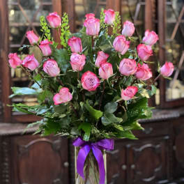 Pink roses arranged in a clear glass vase with a purple ribbon