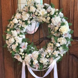 Large white floral wreath on a stand with a ribbon bow