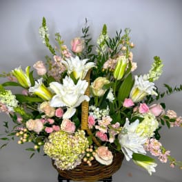 Basket arrangement of white lilies, pink roses, and pale blooms