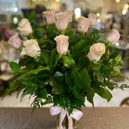 Bouquet of pale pink roses in a clear glass vase with a pink ribbon