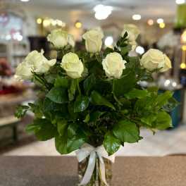 White roses arranged in a clear glass vase with a white ribbon
