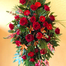Tall standing arrangement of red roses and red daisies with tropical greenery