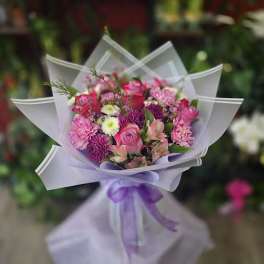 Pink and purple mixed bouquet wrapped in white paper with a purple ribbon