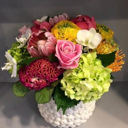 Mixed bouquet with pink rose, orchids, hydrangea, and yellow blooms in a white vase