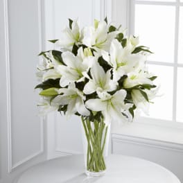 Tall clear vase filled with large white lilies on a round white table