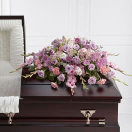 Lavender and pink casket spray of roses and mixed flowers on a dark wood casket