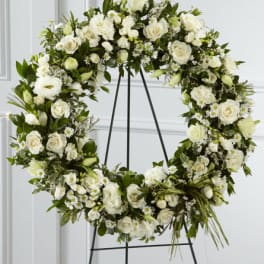 White floral wreath on a black stand with roses and small daisies